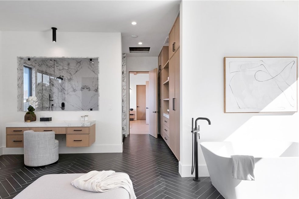 Remodeled master bathroom with a marble-topped floating vanity, large mirror set in a marble surround, freestanding tub, and dark herringbone tile floor by Hillstar Construction