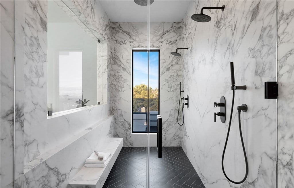Marble walk-in shower with dual rain showerheads, matte-black fixtures, and a picture window by Hillstar Construction