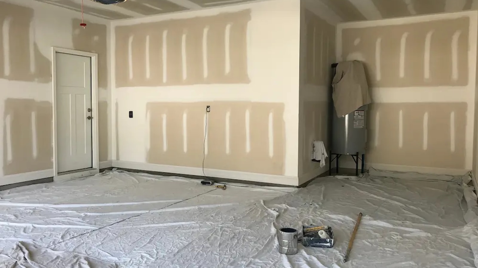 Garage interior mid-conversion with taped and mudded drywall, garage opener overhead, drop cloths on the slab