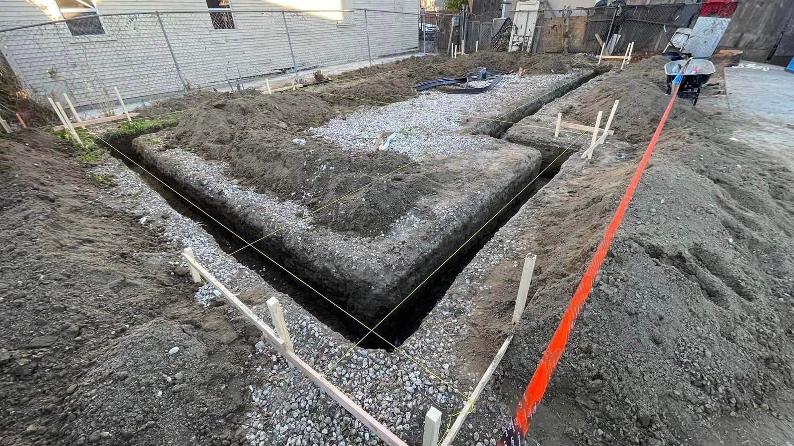 Excavated foundation footing trenches laid out with batter boards and taut string lines alongside an older house