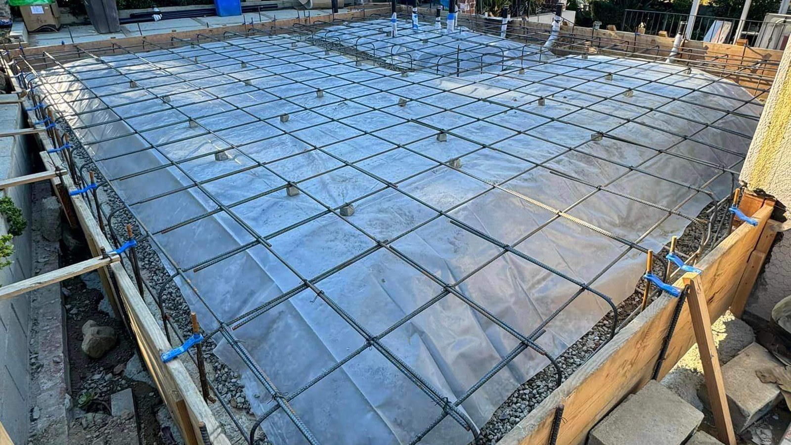 New engineered foundation ready for concrete, with a tied rebar grid over vapor barrier, perimeter forms, and anchor hardware set in place