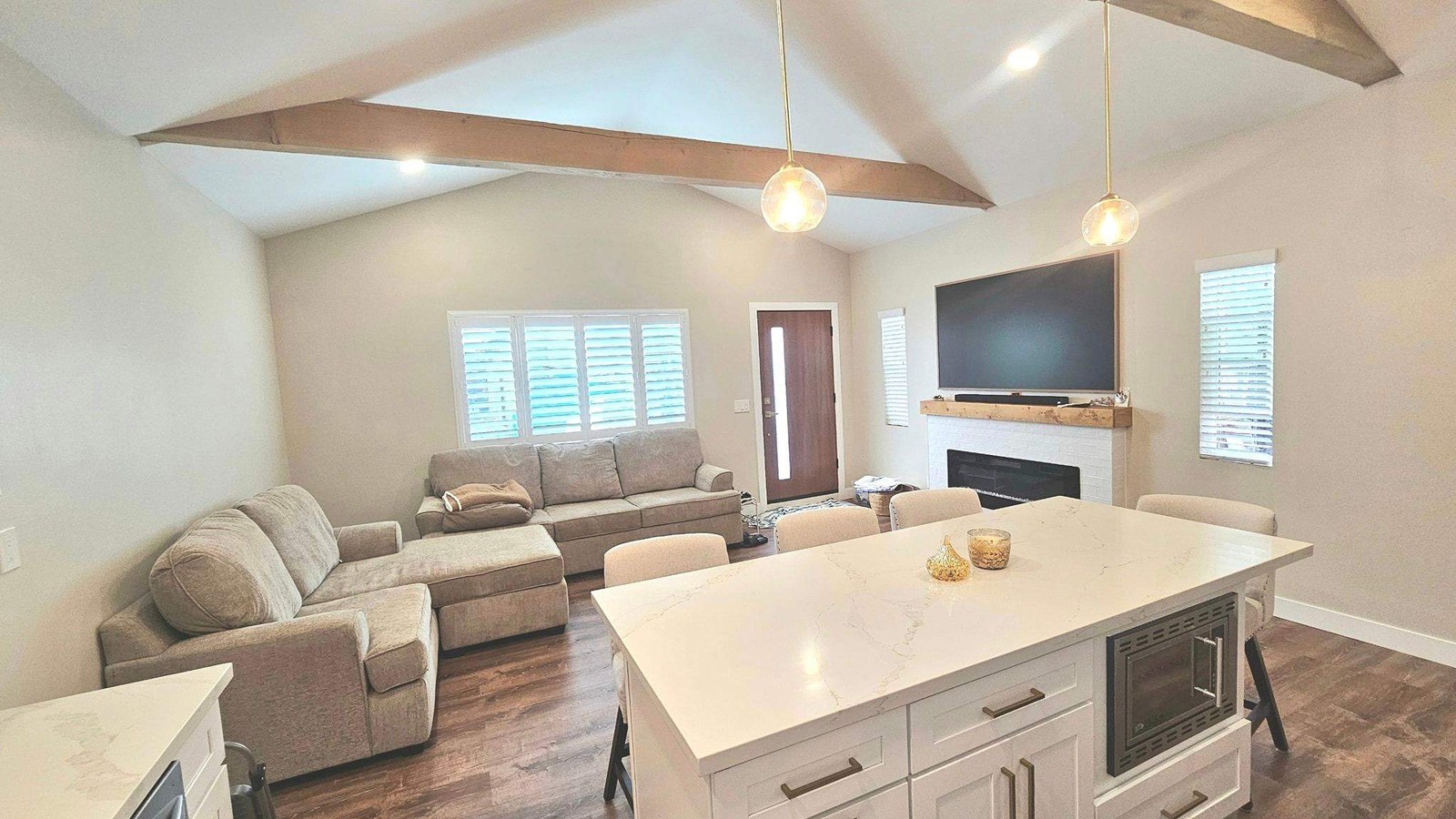 Finished open-plan living and kitchen area after remodeling, with exposed wood ceiling beams, a quartz waterfall island, and new plank flooring