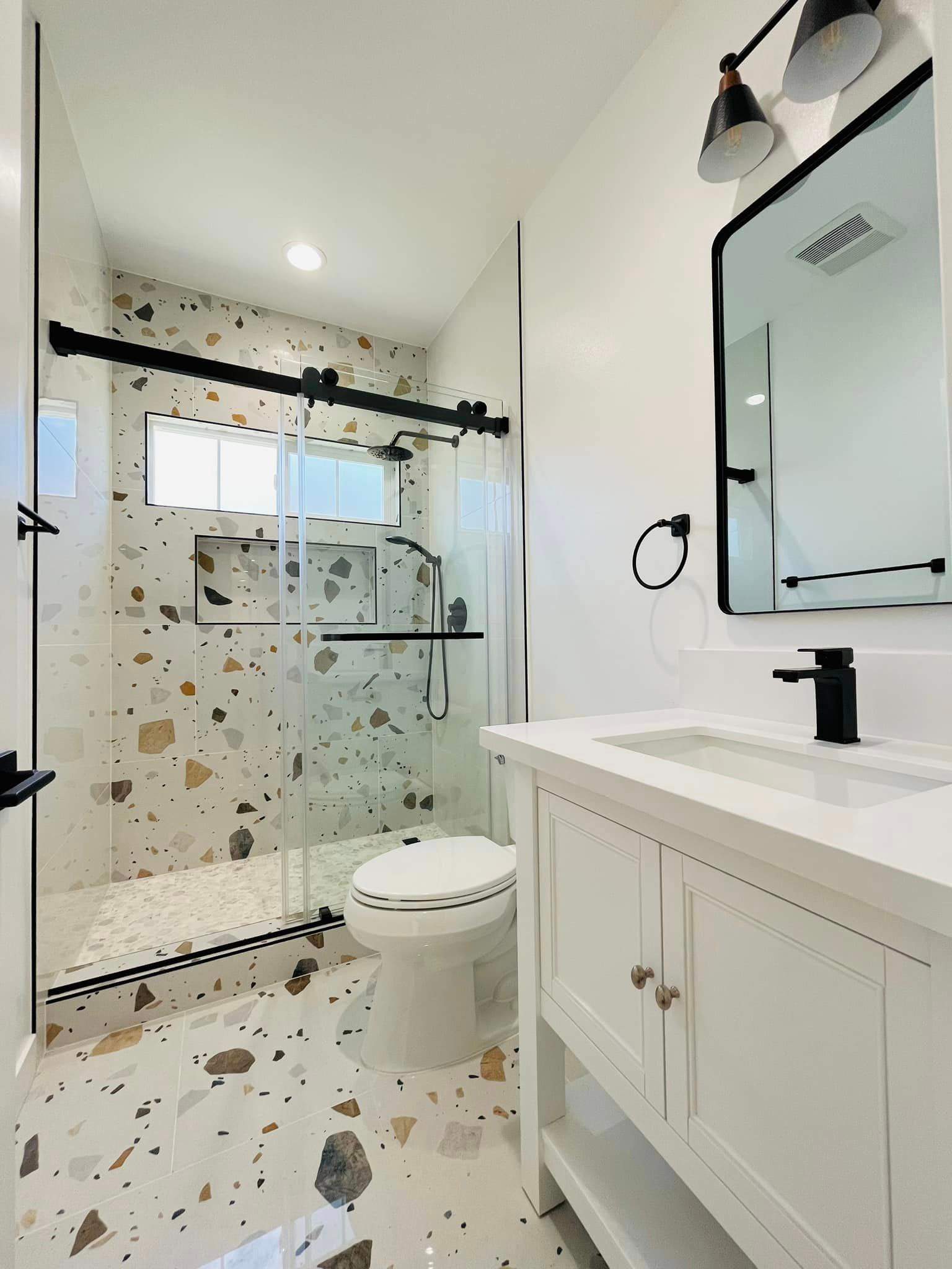 Remodeled bathroom with terrazzo-look tile, a glass sliding-door walk-in shower, toilet and white vanity