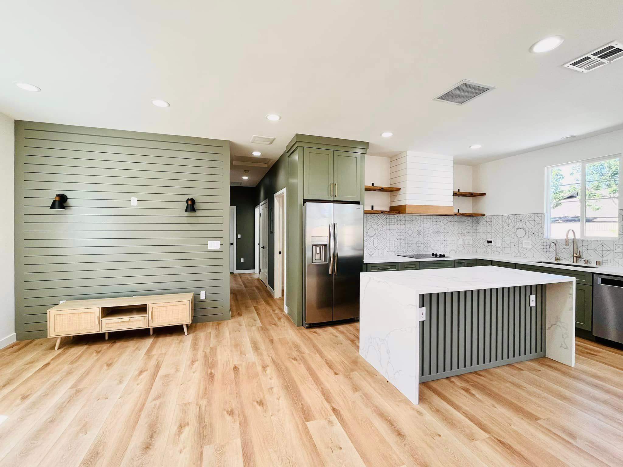 Finished single-story home remodel with an open living area flowing into a green-cabinet kitchen with a white island