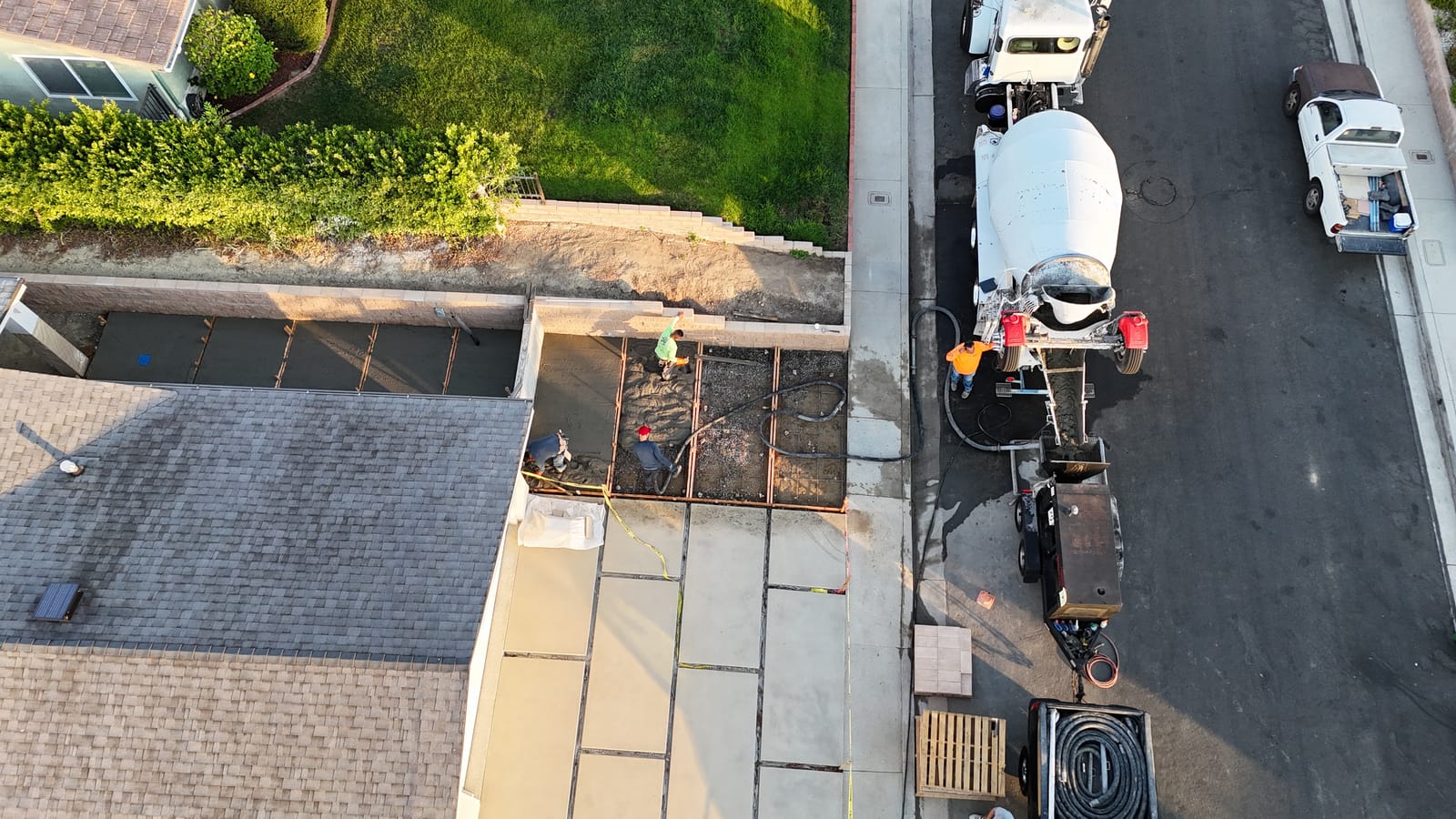 Aerial view of a concrete pour: a mixer truck feeding a pump while the crew places a residential driveway