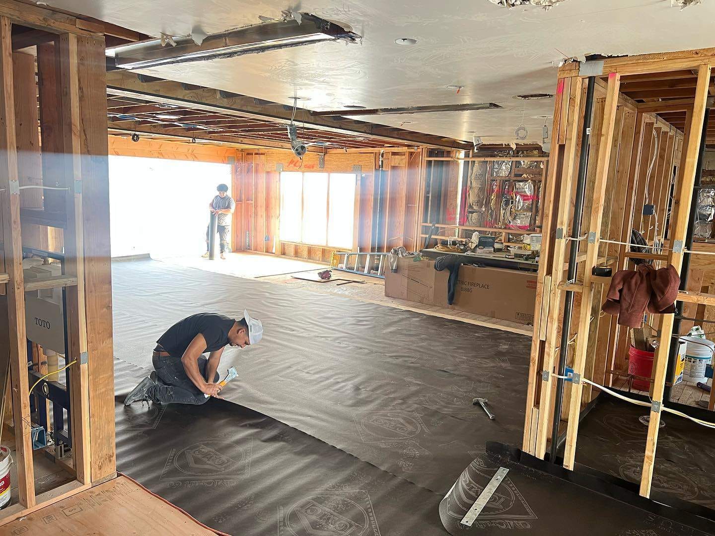 Garage interior stripped to the framing during a Hillstar Construction Inc conversion, with new sheathing and moisture barrier work under way
